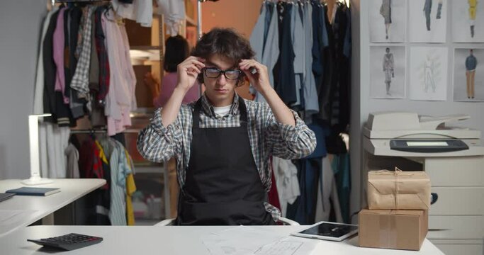 Portrait of young male designer in glasses sitting at desk in warehouse