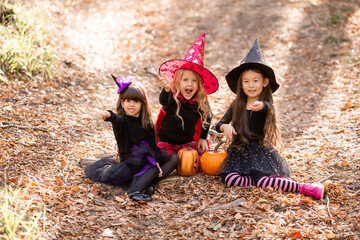 three little girls in witch costumes laugh, conjure, walk through the autumn forest with baskets...