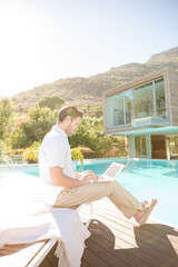 Fototapeta premium Man using laptop at poolside