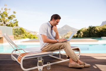 Man using laptop on lounge chair at poolside