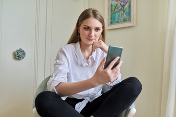 Emotional young beautiful woman looking at smartphone screen