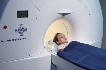 Cute little girl covered with blue towel lying on long table while undergoing mri scan procedure - obrazy, fototapety, plakaty