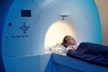 Little patient under blue towel lying on long table of mri scan machine in medical lab - obrazy, fototapety, plakaty