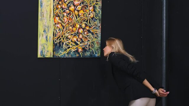 young blonde woman is viewing picture of modern artist in art gallery