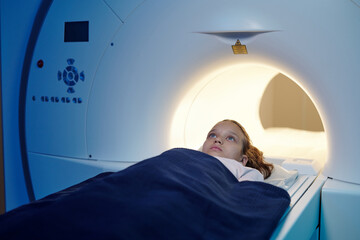 Adorable child lying on table while moving into mri scan machine before medical examination - obrazy, fototapety, plakaty
