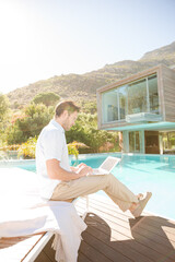 Fototapeta premium Man using laptop at poolside