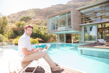 Man using laptop at poolside