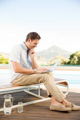 Man using laptop on lounge chair at poolside