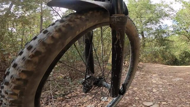 Riding an off road mountain bike front wheel point of view on a gravel path in a forest