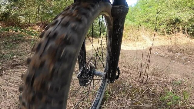Off road front wheel point of view of a mountain bike riding on a forest path downhill