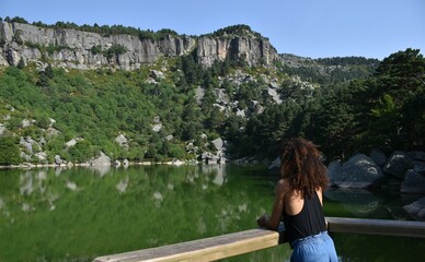 Fototapeta premium Racialized woman with afro hair observing from the viewpoint the beauty of the Black Lagoon. Located in the province of Soria, Spain.