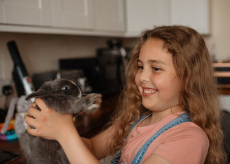 smiling girl with long curly hair in jeans playing with a rabbit at home