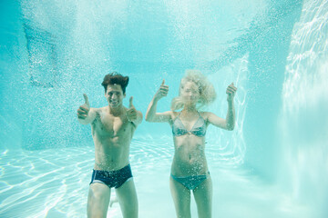 Couple giving thumbs up underwater in swimming pool