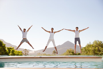 People jumping with arms and legs outstretched at poolside