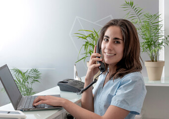 mujer joven trabajando en la recepción de un consultorio odontológico habla por telefono sonriendo