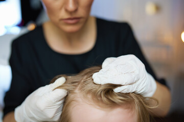 Woman trichologist in rubber gloves checking child hair