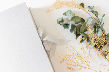 Wedding or family photo album on a light grey box, eucalyptus branches and leaves isolated on white background. Flat lay, top view,