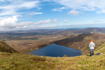 Girl is standing on the top of the mountain. View from behind.. Heart shaped Lake Ouler Tonelagee Mountain, Wicklow County, Ireland.