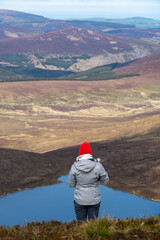 Fototapeta na wymiar Girl is standing on the top of the mountain. View from behind.. Heart shaped Lake Ouler Tonelagee Mountain, Wicklow County, Ireland.