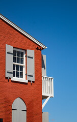 Small window with wooden shutters on the corner of an old red house.