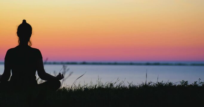 Girl's silhouette sitting in yoga asana at the sea bank on the gradient sunset