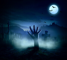 Halloween, dead hand coming out of the ground soil in the cemetery under a full moon - creepy - scary - spooky