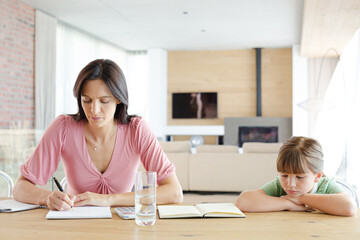 Mother sitting at table with daughter, using calculator