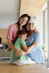 Three generations of women hugging in kitchen