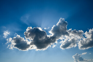 The sun shining behind the white clouds. Blue sky at summer day. Dramatic cloudscape. 