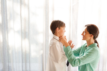 Mother tying son's tie at window