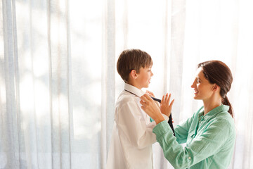 Obraz premium Mother tying son's tie at window