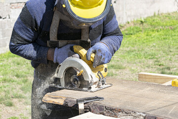 Carpenter cutting wood with a circular saw.
He is wearing a work uniform that provides him with safety.