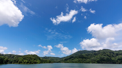 Fototapeta na wymiar White clouds in blue sky over green mountains covered with rainforests trees Beautiful landscape of Mountain and Lake with reflex in the water scenery beautiful view with blue sky and white clouds.