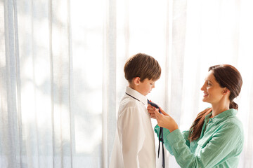 Obraz premium Mother tying son's tie at window