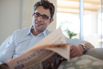 Man reading newspaper on sofa