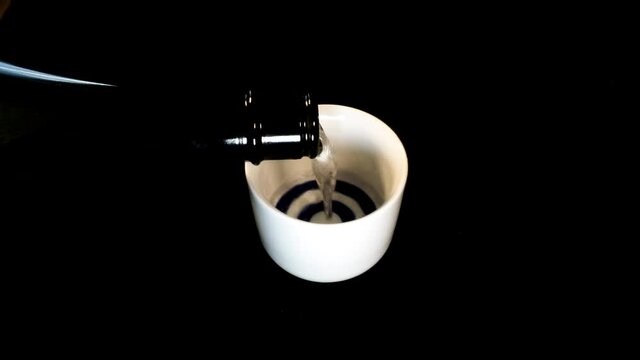 Tokyo,Japan - August 30, 2021: Pouring sake from a big sake bottle into small round ceramic sake cup or small kiki-choko
