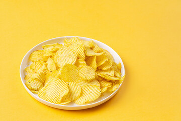 White plate with golden crinkled chips on yellow background with copy space. Colors of Year 2021.