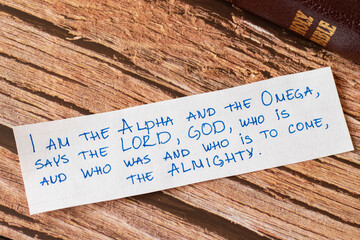 God Jesus Christ is the I AM, Alpha and Omega, First and Last, the LORD Almighty. Closeup of handwritten message on wooden background with closed Bible. Biblical concept book of Revelation. - obrazy, fototapety, plakaty