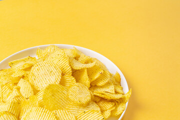 White plate with golden crinkled chips on yellow background with copy space. Colors of Year 2021. Close-up of chips.