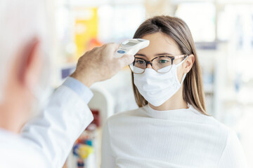 Measurement of body temperature with a digital thermometer, protection against corona virus. A close-up shot of a woman's upper body with eyeglasses and a protective mask on her face. Health check