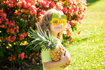 Happy smiling kid boy holds pineapple in hands, child and tropical fruits.