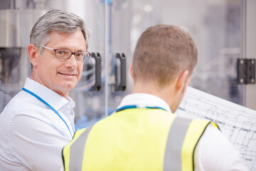 Obraz premium Supervisor and worker reading blueprints in factory