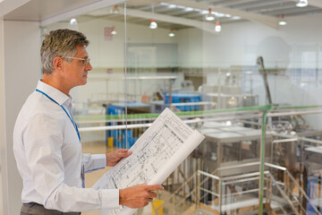Businessman reading blueprints in factory