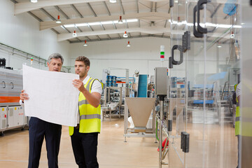 Supervisor and worker reading blueprints in factory