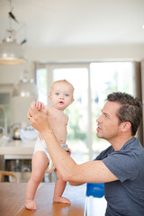 Father helping baby walk on table