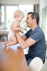 Father helping baby walk on table
