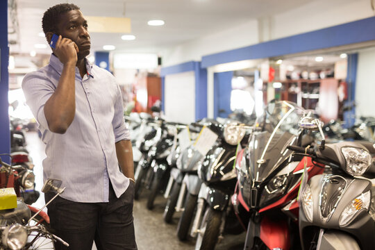Serious afro american talking on mobile phone in motorcycle salon. High quality photo