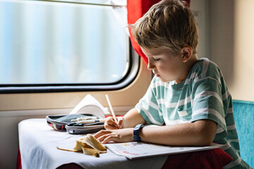 Focused male kid drawing writing paper notes enjoying travel by train at luxury railway carriage