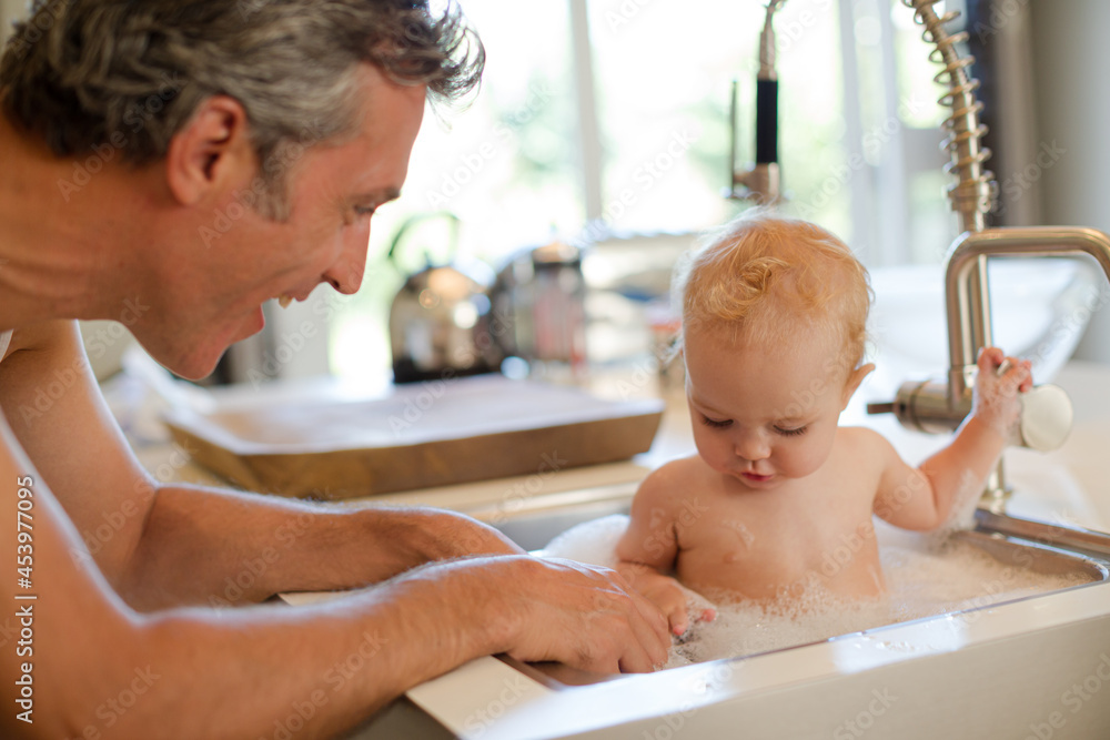 Wall mural father bathing baby in kitchen sink