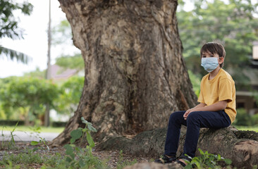 Fototapeta premium Child wearing face mask sitting under big tree and looking at camera.Pollution concept.
